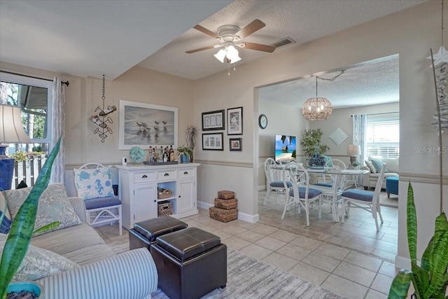 living area with visible vents, ceiling fan with notable chandelier, a textured ceiling, light tile patterned flooring, and baseboards