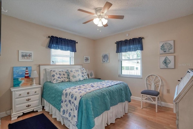 bedroom featuring light wood-type flooring, baseboards, a textured ceiling, and a ceiling fan