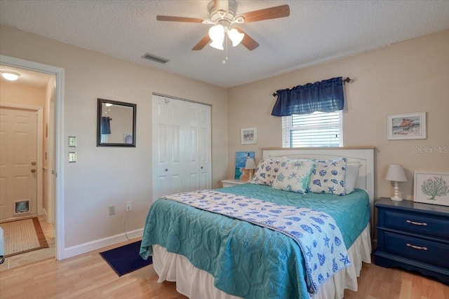 bedroom featuring baseboards, visible vents, light wood-style floors, a closet, and a textured ceiling