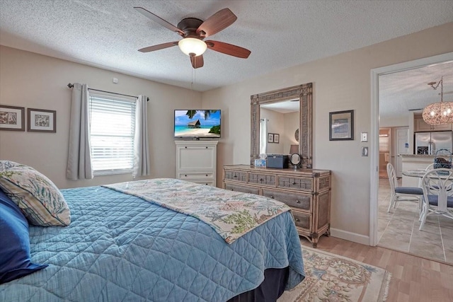 bedroom featuring ceiling fan with notable chandelier, stainless steel fridge with ice dispenser, light wood-style floors, and a textured ceiling