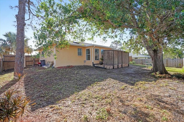 back of property featuring an outdoor structure, a storage unit, a fenced backyard, and stucco siding