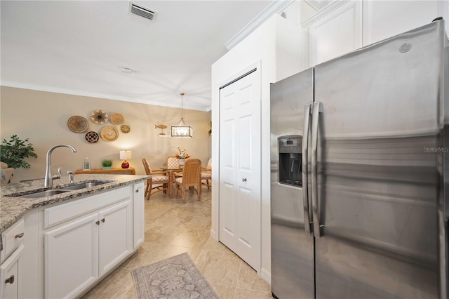 kitchen with crown molding, visible vents, white cabinets, a sink, and stainless steel fridge