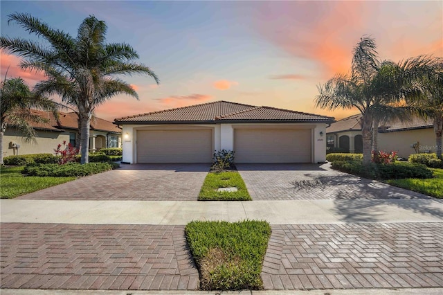 view of front of house featuring a garage, decorative driveway, a tile roof, and stucco siding