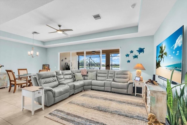 living area featuring a raised ceiling, light tile patterned floors, ceiling fan with notable chandelier, and visible vents