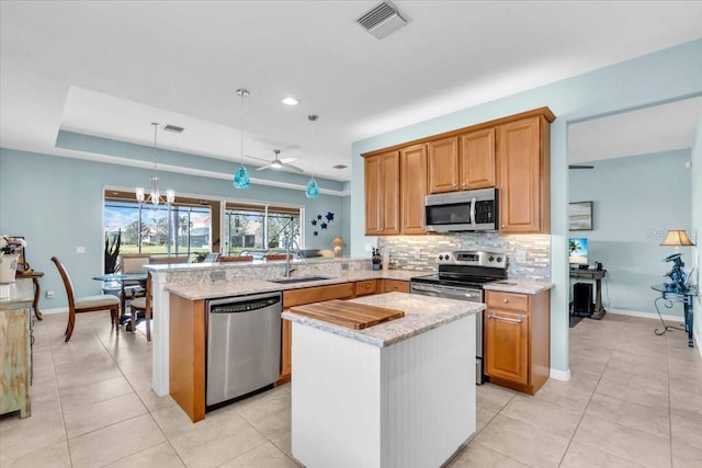 kitchen with visible vents, a peninsula, a sink, decorative backsplash, and appliances with stainless steel finishes