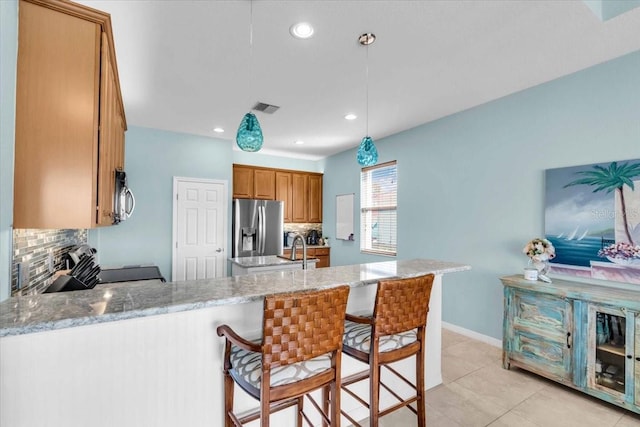 kitchen with visible vents, tasteful backsplash, stainless steel appliances, a peninsula, and brown cabinetry