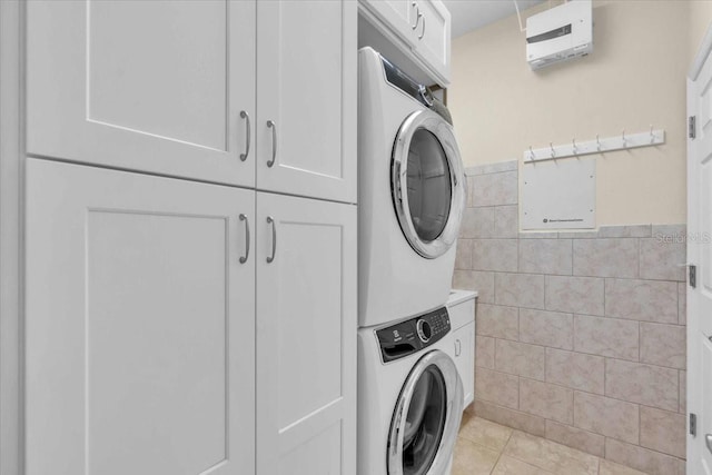 washroom with stacked washer and dryer, wainscoting, light tile patterned flooring, cabinet space, and tile walls