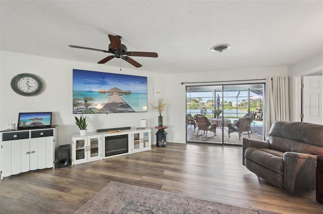 living room with a ceiling fan, a fireplace, visible vents, and wood finished floors