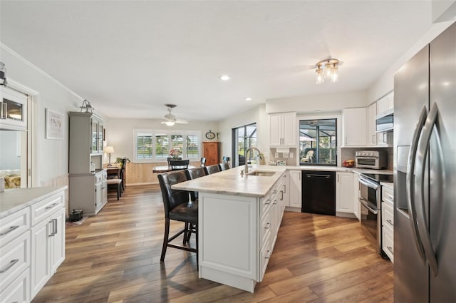 kitchen with a breakfast bar, light wood-style flooring, appliances with stainless steel finishes, a healthy amount of sunlight, and a sink