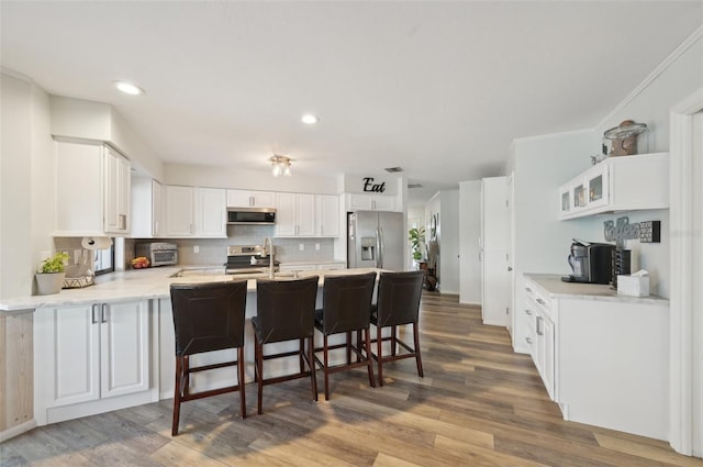 kitchen featuring appliances with stainless steel finishes, white cabinetry, a peninsula, and wood finished floors