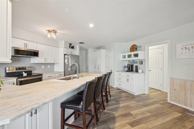 kitchen with stainless steel appliances, white cabinetry, a sink, wood finished floors, and a kitchen breakfast bar