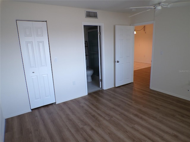 unfurnished bedroom with a closet, wood finished floors, visible vents, and connected bathroom