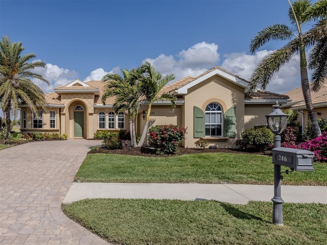 mediterranean / spanish-style home featuring a tile roof, a front lawn, decorative driveway, and stucco siding