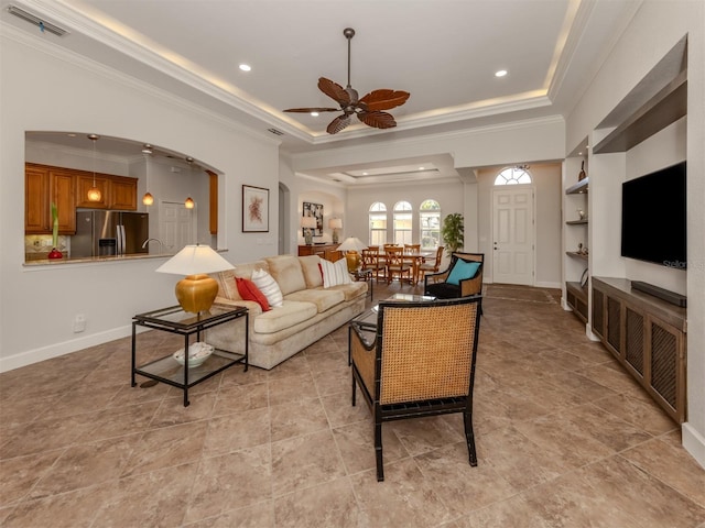 living room with ornamental molding, a tray ceiling, visible vents, and arched walkways