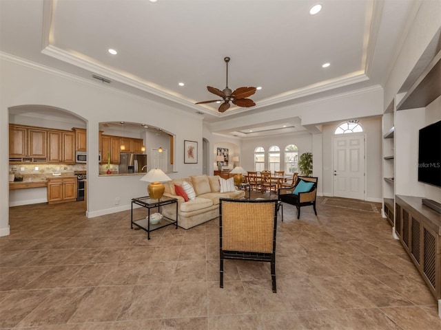 living room featuring baseboards, ceiling fan, a tray ceiling, crown molding, and recessed lighting