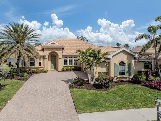 mediterranean / spanish-style house with a garage, a tiled roof, decorative driveway, a front lawn, and stucco siding