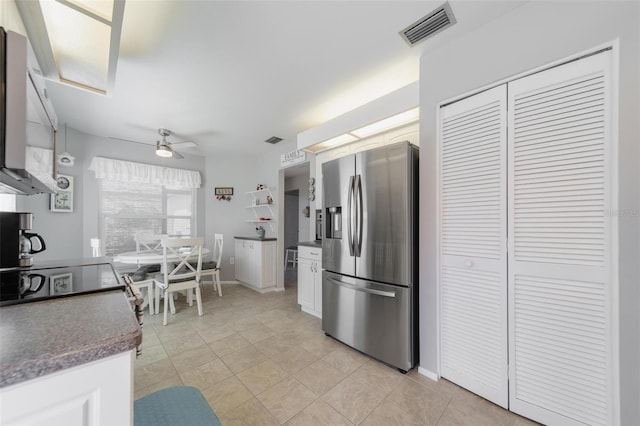 kitchen with dark countertops, visible vents, light tile patterned flooring, ceiling fan, and stainless steel fridge with ice dispenser