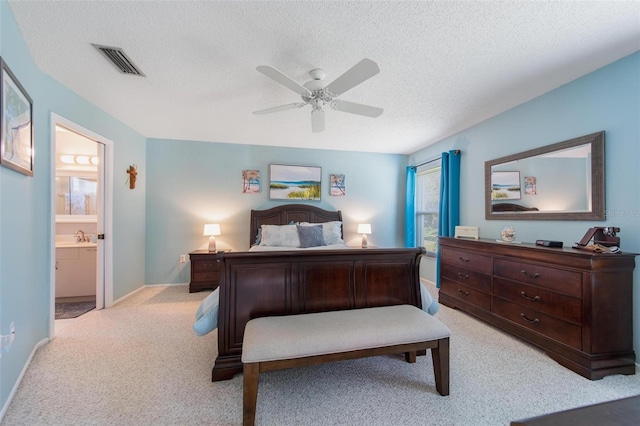 bedroom with a textured ceiling, ceiling fan, light colored carpet, visible vents, and ensuite bath