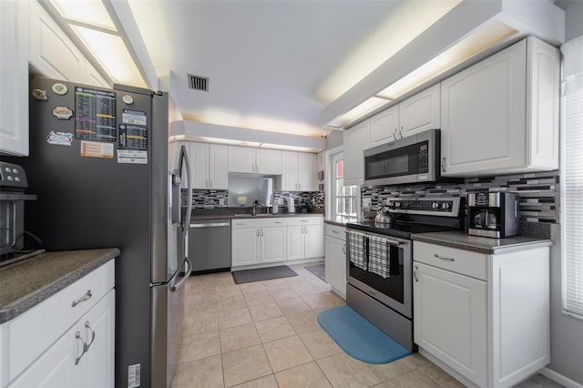 kitchen featuring stainless steel appliances, a sink, white cabinets, decorative backsplash, and dark countertops