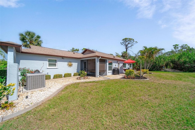 rear view of house with a sunroom, stucco siding, a lawn, and central AC unit