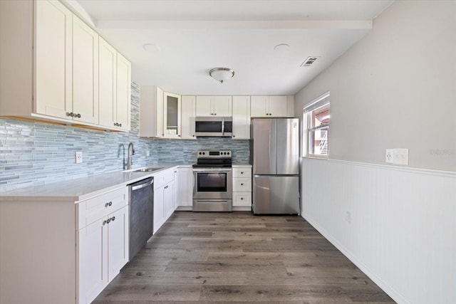 kitchen with stainless steel appliances, wood finished floors, a sink, visible vents, and wainscoting