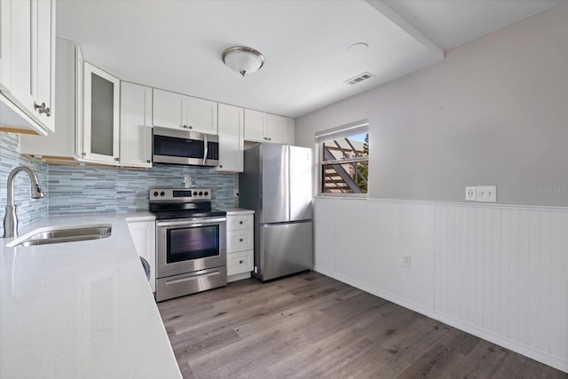 kitchen with light wood finished floors, white cabinets, stainless steel appliances, light countertops, and a sink