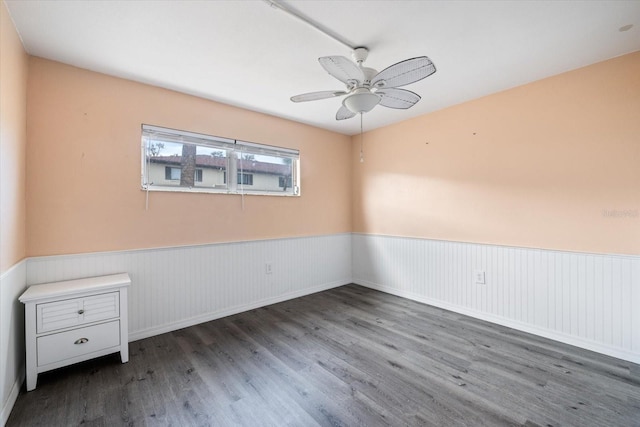 empty room with a wainscoted wall, wood finished floors, and a ceiling fan