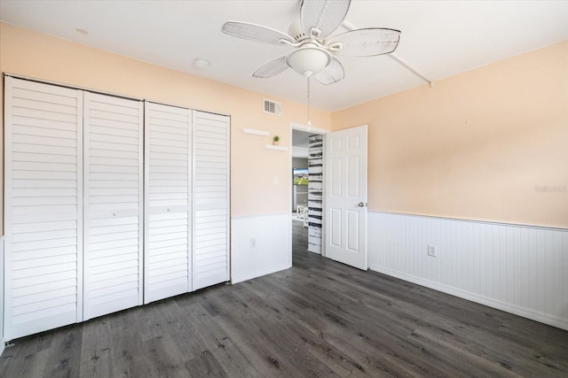 unfurnished bedroom with visible vents, wainscoting, ceiling fan, dark wood-style flooring, and a closet