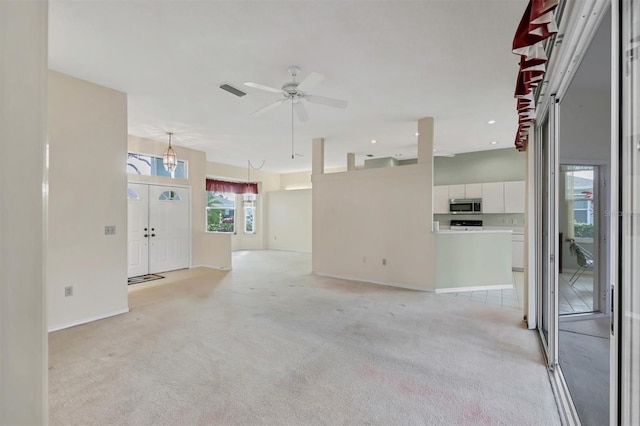 unfurnished living room with baseboards, visible vents, a ceiling fan, and light colored carpet