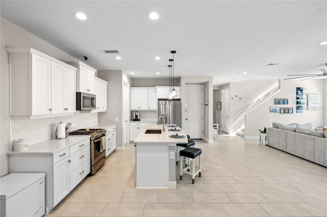 kitchen with a breakfast bar, stainless steel appliances, a ceiling fan, open floor plan, and a sink