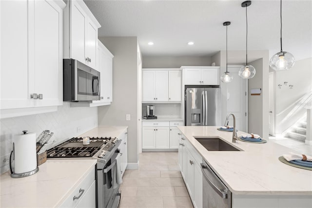 kitchen with stainless steel appliances, a sink, white cabinets, backsplash, and an island with sink