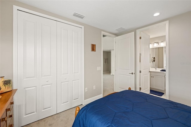 bedroom with a closet, light colored carpet, visible vents, ensuite bath, and baseboards