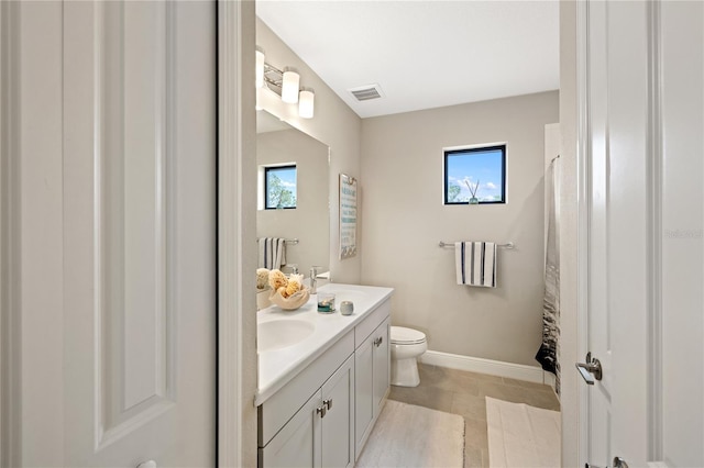 bathroom with double vanity, baseboards, visible vents, toilet, and a sink