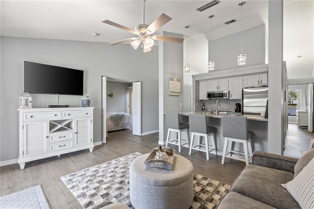 living area with a ceiling fan, lofted ceiling, a textured ceiling, and wood finished floors