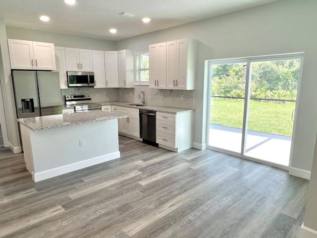 kitchen with light wood finished floors, tasteful backsplash, white cabinets, stainless steel appliances, and a sink