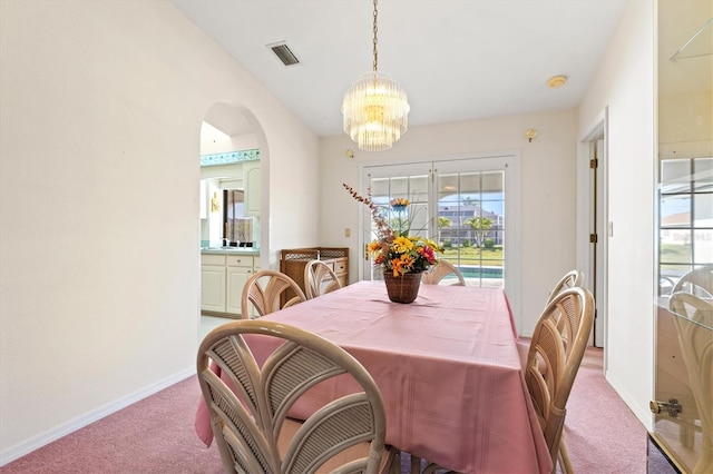 carpeted dining room featuring a notable chandelier, visible vents, arched walkways, and baseboards