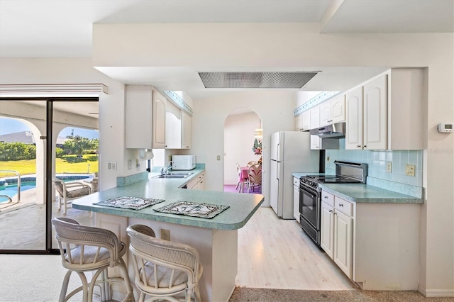 kitchen with under cabinet range hood, a breakfast bar, decorative backsplash, electric range, and a sink