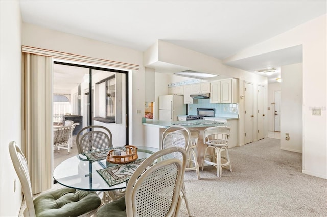 dining room with light colored carpet, lofted ceiling, and baseboards