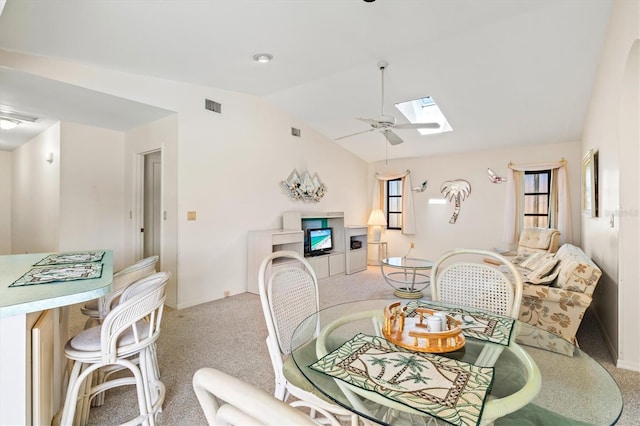 dining space with visible vents, a ceiling fan, vaulted ceiling with skylight, a fireplace, and light colored carpet