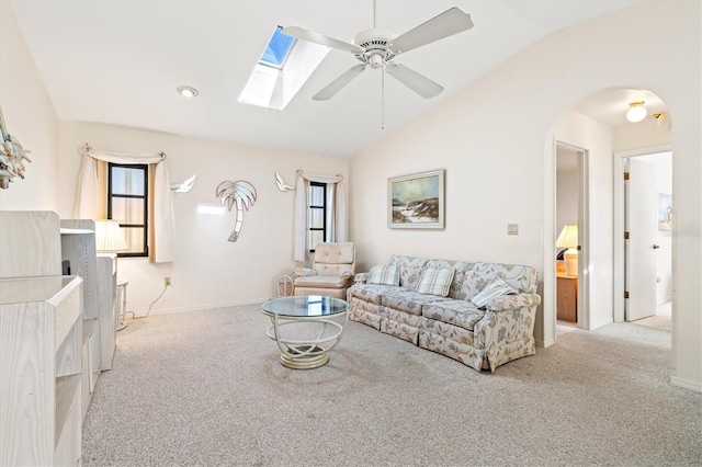 living room featuring lofted ceiling with skylight, light colored carpet, ceiling fan, and arched walkways