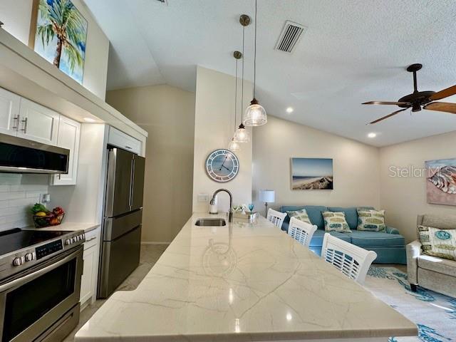 kitchen with visible vents, open floor plan, vaulted ceiling, stainless steel appliances, and a sink