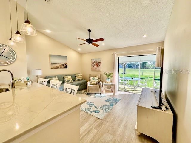 living area with lofted ceiling, recessed lighting, light wood-style floors, ceiling fan, and a textured ceiling