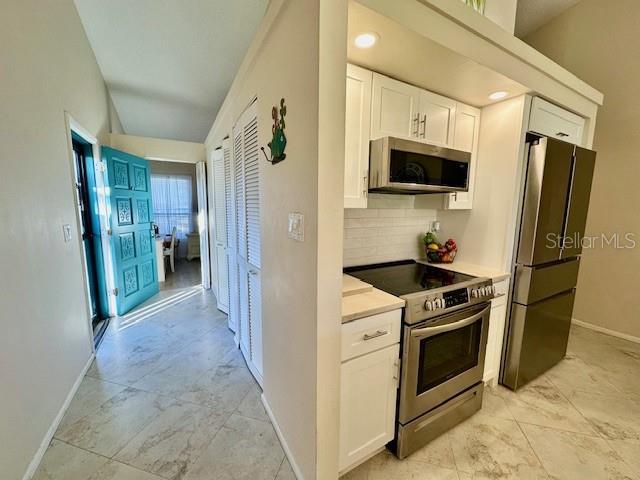 kitchen featuring stainless steel appliances, tasteful backsplash, light countertops, white cabinets, and baseboards