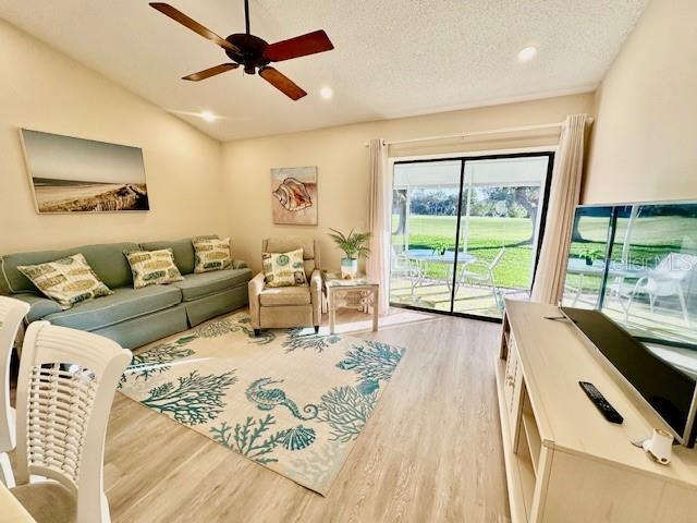 living area featuring lofted ceiling, ceiling fan, a textured ceiling, light wood-style flooring, and recessed lighting