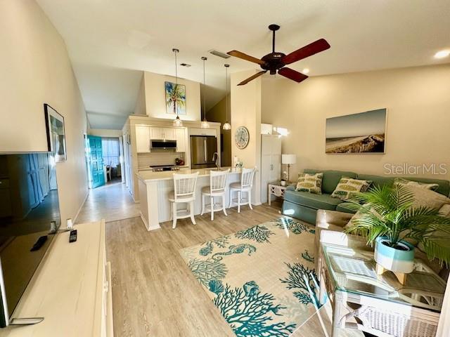 living area with light wood-style floors, ceiling fan, and high vaulted ceiling