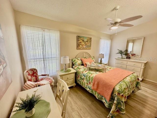 bedroom with light wood-type flooring, multiple windows, vaulted ceiling, and a textured ceiling