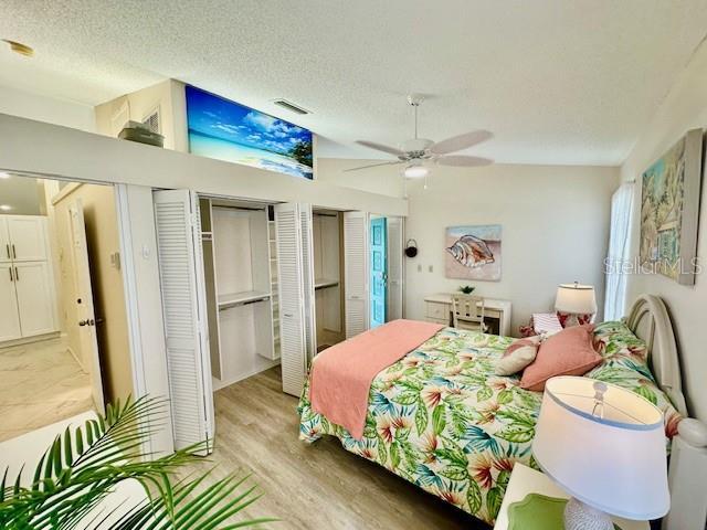 bedroom with a textured ceiling, two closets, visible vents, and light wood-style floors