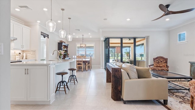 living area with crown molding, light tile patterned floors, visible vents, a ceiling fan, and baseboards