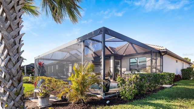 back of house featuring a lanai, a lawn, a tiled roof, and stucco siding