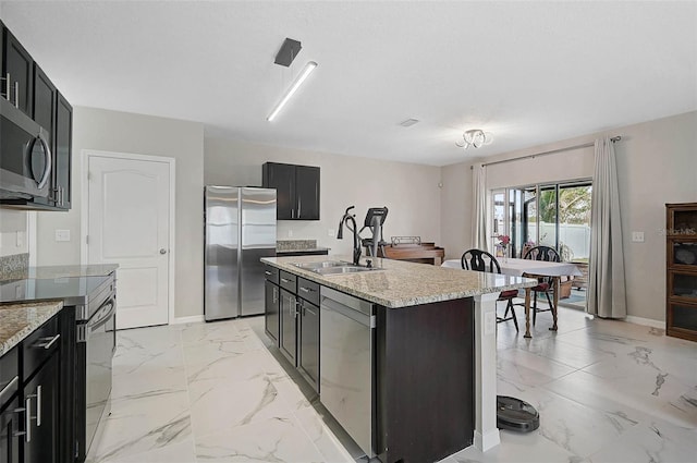 kitchen with marble finish floor, stainless steel appliances, a sink, and a kitchen island with sink